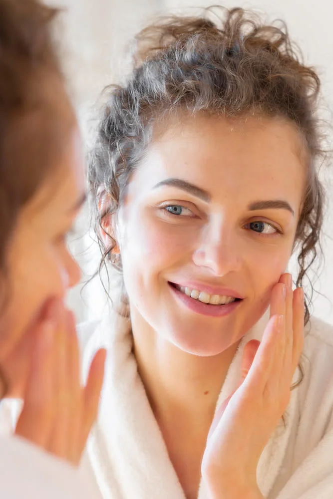 happy mature woman woman-applying-cream-face-while-looking-mirror